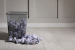 © New Africa - Trash bin with paper on floor near white wall, space for text. Recycling rubbish
