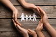 Parents and child protecting paper cutout of family at wooden table, top view