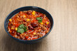 Bowl with tasty chili con carne on wooden table, closeup