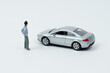 © Dzmitry - On a white surface is a car and a miniature figurine of a man looking at the car.