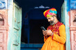 Happy north Indian mature man wearing colorful outfits and turban using smart phone, Smiling Traditional male calling on android smart mobile phone.