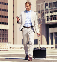 This app is convenient for a businessman on the go. Shot of a young businessman using a cellphone while walking with a suitcase in the city.