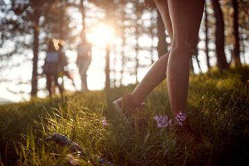 Woman legs, walking in forest with friends in the background. Outdoor in forest on sunny day. Sport, lifestyle, fashion concept.