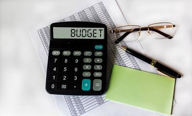 Budget concept. The text of the budget on the calculator lies on financial documents, next to it are glasses, a pen and stickers for writing.