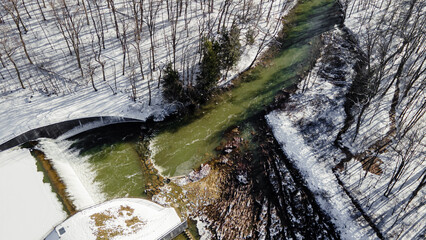 Wall Mural - Aerial beautiful landscape view of a snowy bridge on snow lands, river and trees in the forest