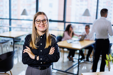 A young woman in a black shirt with bright emotions on her face, she stands against the background of her colleagues and gesticulates with her hands