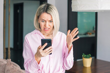 Middle-aged Woman Holding Phone, Reading Unpleasant News In Social Media
