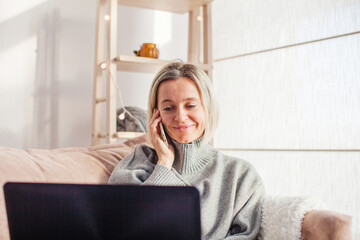 Wall Mural - Happy middle aged woman using her laptop on the sofa at home