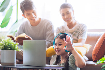 happiness asian child daughter wear headphone online study during homeschooling asian mother and father enjoy watching on sofa couch at home ,home quarantine, online learning new normal lifestyle