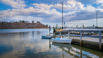 Cumulous clouds and water reflections at Harwich harbor with empty boats and dinghy mooring tied to the commercial dock.