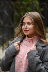 Poster - Fashionable and beautiful young woman 16-20 years old, dressed in an pink knitted sweater, glasses, dark skirt and a gray classic trench coat.