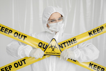 Epidemiologist woman in protective clothing is in a restricted area with a danger sign. Yellow line Keep Out Quarantine. Quarantine alert sign.