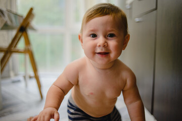 Portrait of a naked child. The baby stands and looks at the camera. Smiling, laughing, Indulging