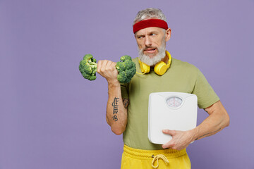 Wall Mural - Sceptic confused elderly gray-haired bearded man 40s years old in headband khaki t-shirt hold look at broccoli dumbbell floor scales isolated on plain pastel light purple background studio portrait.