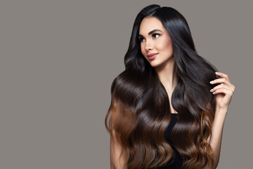 Brunette woman with black wavy ombre hair. Portrait on a gray background