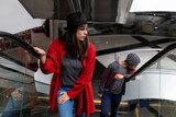 Fototapeta  - Two young Latin American brothers walk up escalators in a shopping mall. She wears a black hat and red sweater, he wears a hat and gray sweater. Walking and leisure concept.