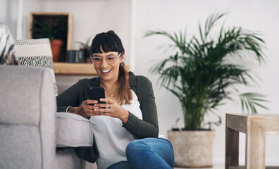 Sticker - Technology keeps us connected. Cropped shot of an attractive young woman sitting in her living room alone and using her cellphone.