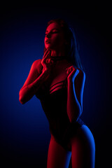 Beautiful young brunnete girl standing in sexy lingerie in colored light in studio on a dark background