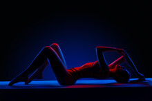 Beautiful Young Brunnete Girl Lying In Sexy Lingerie In Colored Light In Studio On A Dark Background