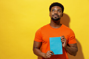 Wall Mural - Young dreamful minded pensive man of African American ethnicity 20s wear orange t-shirt hold book diploma look overhead isolated on plain yellow background studio portrait. People lifestyle concept.