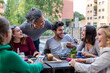 © MandriaPix - group of multiethnic friends having breakfast with coffee, cappuccino and chocolate muffin, meeting of young people outdoors at a coffee shop