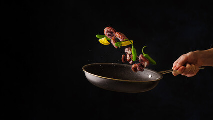 Sea food. Seafood - octopus with vegetables in a frozen flight in a pan on a black background. there are no people in the photo. Restaurant, hotel. Advertising, banner.