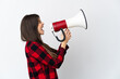 © luismolinero - Teenager Brazilian girl isolated on white background shouting through a megaphone to announce something in lateral position
