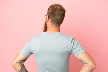 Wall Mural - Young reddish caucasian man isolated on pink background in back position and looking side