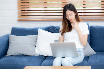 Wall Mural - Beautiful young asian woman working on laptop computer and thinking idea on sofa at home, freelance girl sitting on couch using notebook to internet at living room, one person, lifestyle concept.