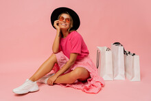 Pretty Smiling Woman In  Spring Trendy Outfit Posing With White Shopping Bags In Studio Over Pink Background.