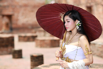 Young fashion and beautiful asian woman wearing Thai white traditional costume with red antique umbrella standing outdoor in ancient temple Ayutthaya, Thailand