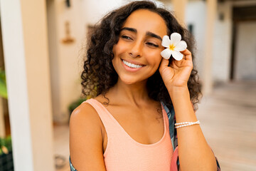 Wall Mural - Close up portrait of  beautiful  woman with tropical flower  in hand posing in luxury spa hotel. Spa and body care concept.