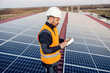 © dusanpetkovic1 - A handyman scrolling on tablet and checking on panels on roof.