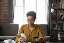 Serious Young Black Bank Customer Woman Paying For Purchase, Domestic Fees, Bills By Blue Plastic Credit Card, Using Online Payment App On Smartphone, Shopping On Internet Stores