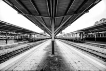 Black And White Railway Station Platform With Metal Platform Roof Where Passenger Trains Are Parked