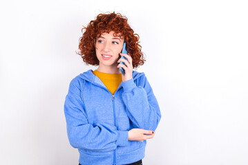 Portrait of a smiling young redhead girl wearing blue jacket over white background talking on mobile phone. Business, confidence and communication concept.