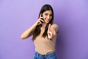 Young caucasian woman using mobile phone isolated on purple background showing and lifting a finger