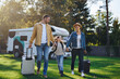 Happy young family walking with suitcases, coming home from caravan trip outdoors in garden