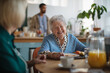 © Halfpoint - Smiling elderly woman enjoying breakfast in nursing home care center.