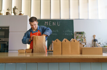 Wall Mural - Cheerful young Down Syndrome waiter working in take away restaurant, social inclusion concept.