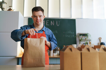 Wall Mural - Cheerful young Down Syndrome waiter working in take away restaurant, social inclusion concept.