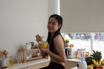 young Asian woman cooking vegetable healthy food and eating or drinking in home kitchen