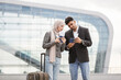 © sofiko14 - Excited Muslim couple with suitcase, standing outdoors at airport and checking their flight schedule, looking at the ticket and smartphone. Business trip together. People, travel, technology concept