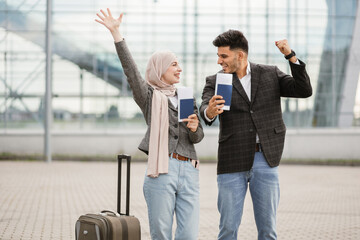 Poster - Smiling Muslim woman in hijab and Arab man, posing on camera outside modern airport terminal, demonstrating their passports and tickets while waiting flight. Ready for trip. Business people