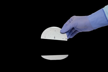 A hand in a rubber glove holds broken multilayer semiconductor silicon wafer with a microcircuit chip of a powerful Darlington transistor isolated on a black background