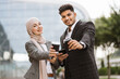© sofiko14 - Smiling business couple, handsome Arab man and Muslim woman in hijab, standing outdoors in the street on coffee break, using phones and drinking take away coffee