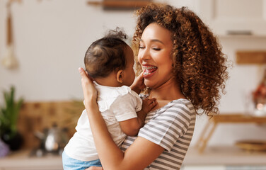 Happy, cheerful ethnic mom holds a laughing baby daughter in her arms.