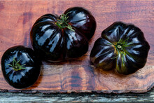 Above View Of American Black Heirloom Tomatoes On Reddish Wood Cutting Board