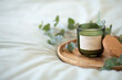 Green scented candle and a branch of eucalyptus on a wooden tray.