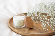 © NesolenayaAleksandra - White scented candle and a branch of gypsophila flowers on a wooden tray.